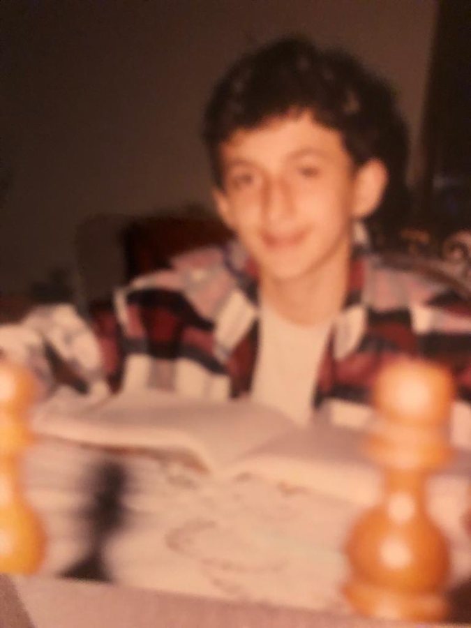 Childhood photograph of Levent Kutlu smiling behind a chessboard